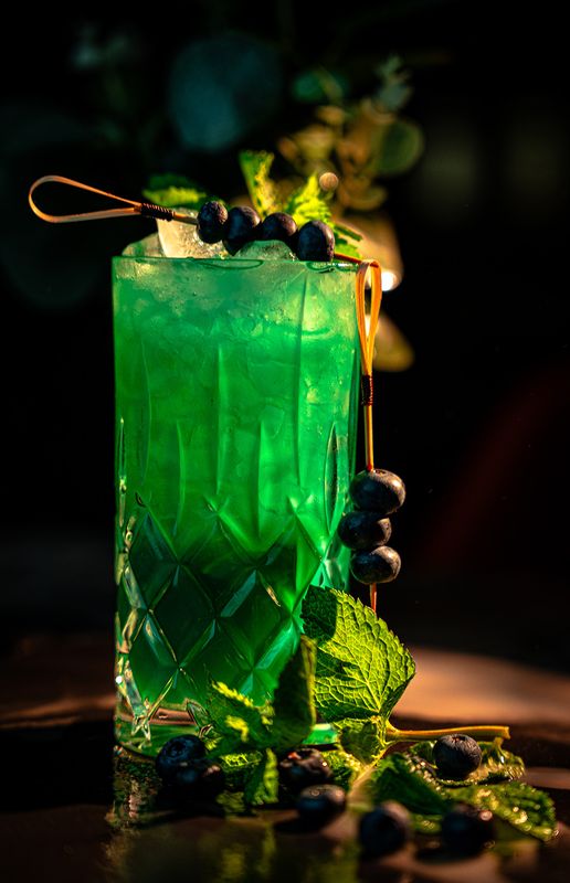 Leuchtend grüner Cocktail im geschliffenen Longdrinkglas mit Blaubeerspieß und Minze