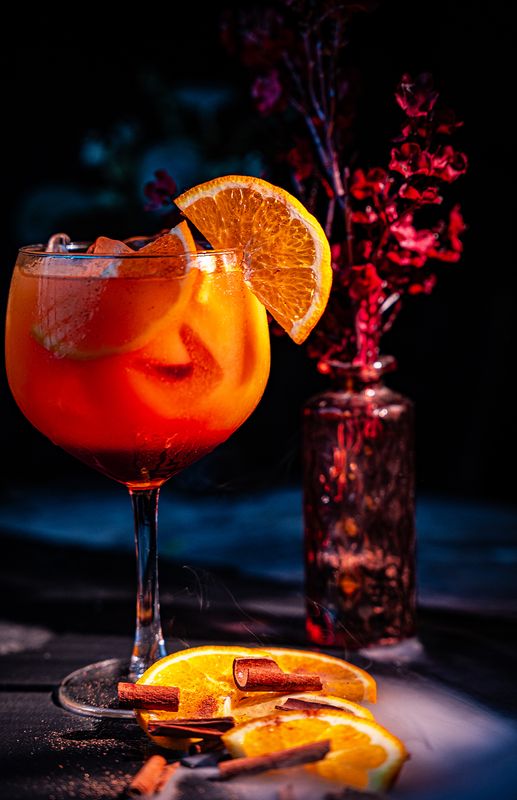 Orangefarbener Spritz im Ballonglas mit Orangenscheibe und Zimtstangen