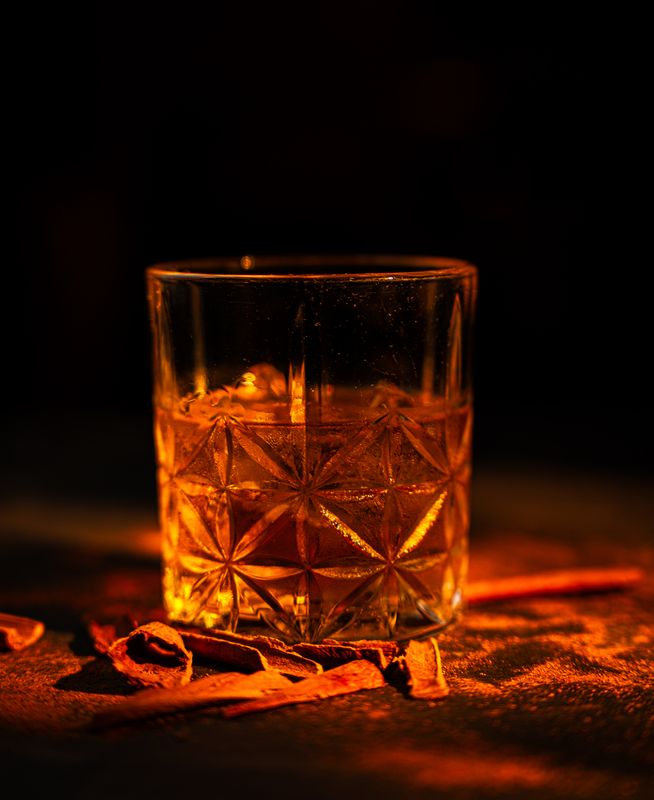 Kristallglas mit bernsteinfarbenem Drink auf Eis, umgeben von Zimtstangen